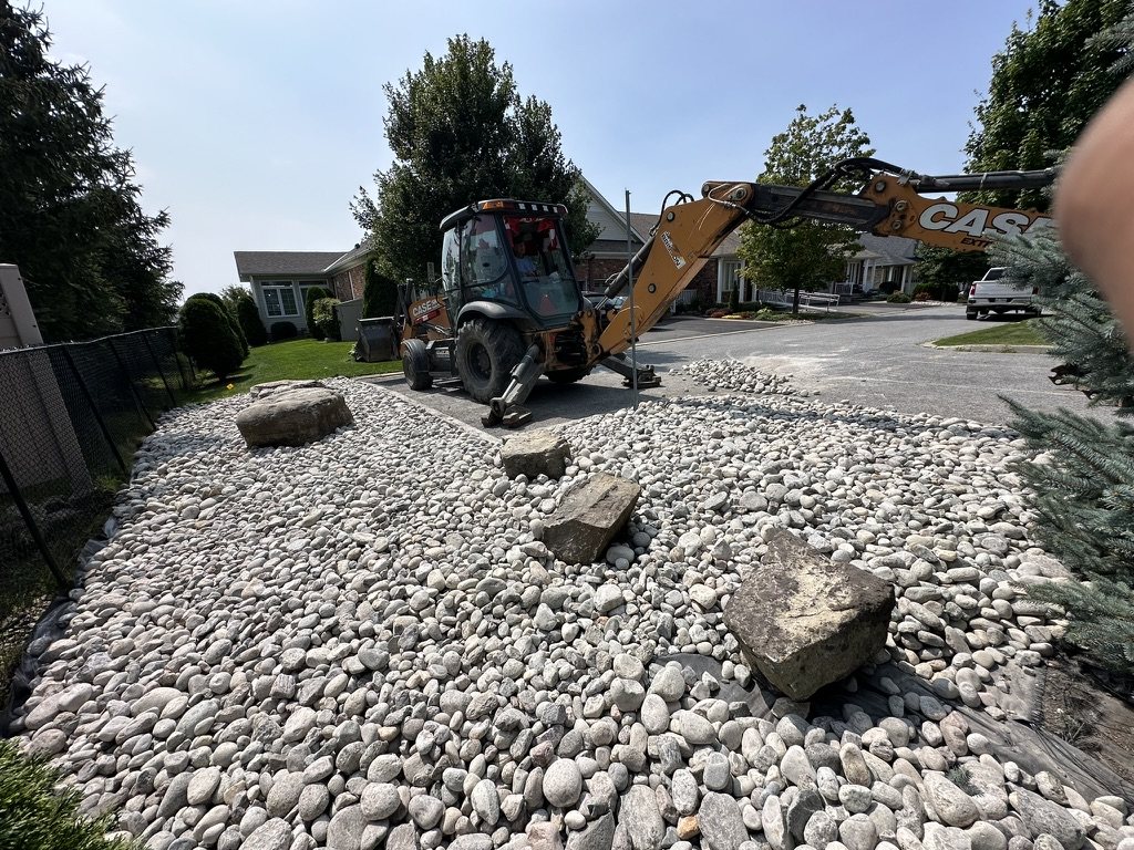 OneBluePlanet Case backhoe installing river rock as part of commercial landscape improvement work