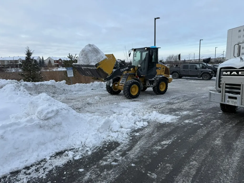 John Deere loader carrying snow at a commercial parking lot