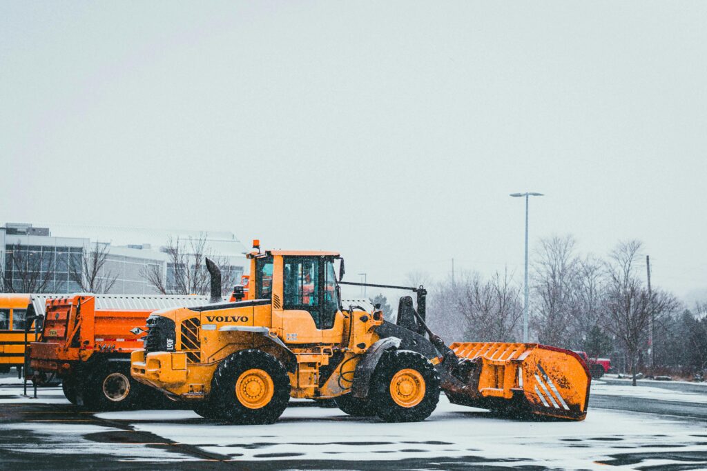 How I Estimate Parking Lot Maintenance Costs in Nepean and Barrhaven A yellow bulldozer by Volvo clearing snow in a winter landscape. Industrial machinery for snow removal.